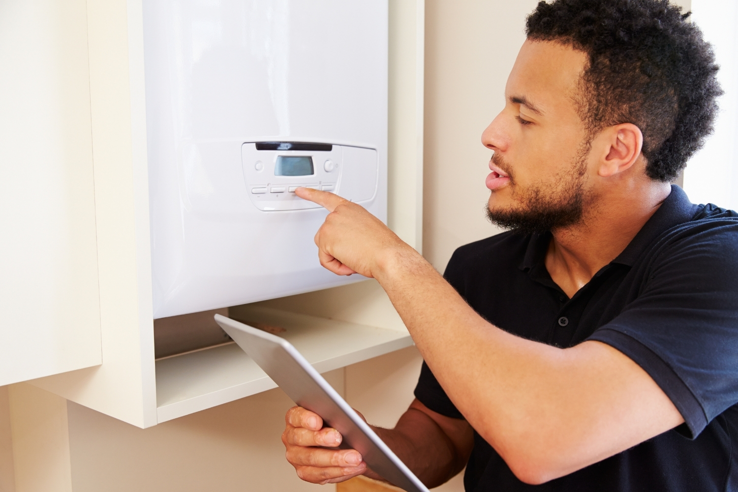 A man pressing a button on the front of a boiler while holding an electronic tablet.